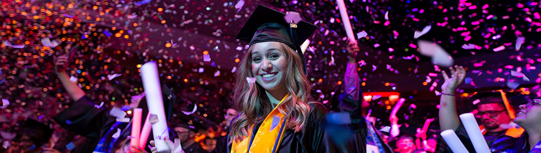 A graduate smiles and waves at PCC graduation ceremony
