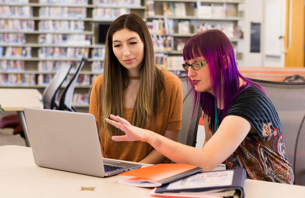 a PimaOnline Navigator assists a student on a laptop in a Pima Library