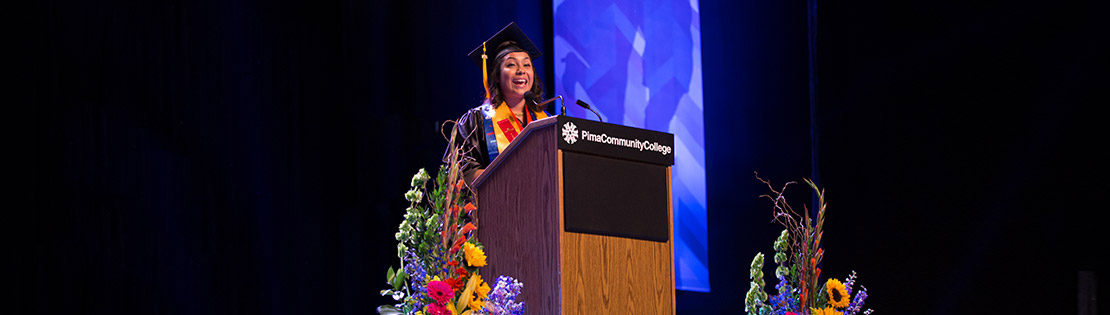 A woman stands speaking at Pima's graduation ceremony