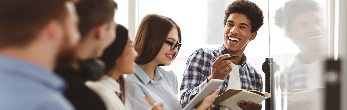 A group of students stand smiling while taking notes at a whiteboard