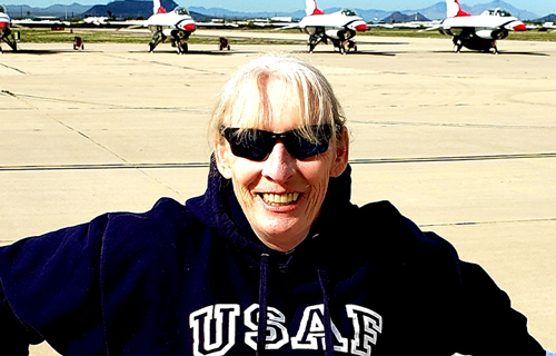 Annette Perkins stands smiling on a military base with jets in the background
