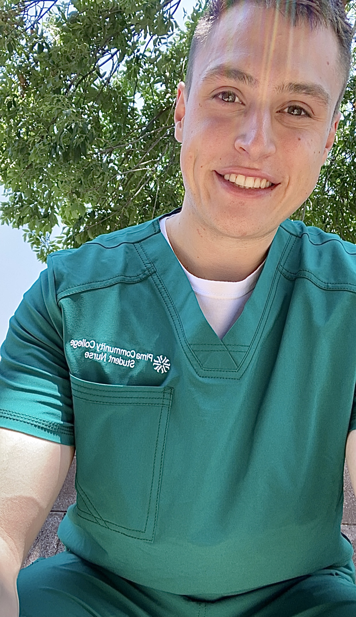 Keaton Baker smiles in front of a tree with green leaves.