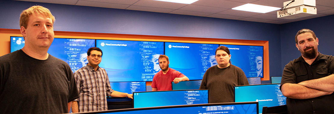 5 students stand in the Cyber Security Center of Excellence posing for a photo