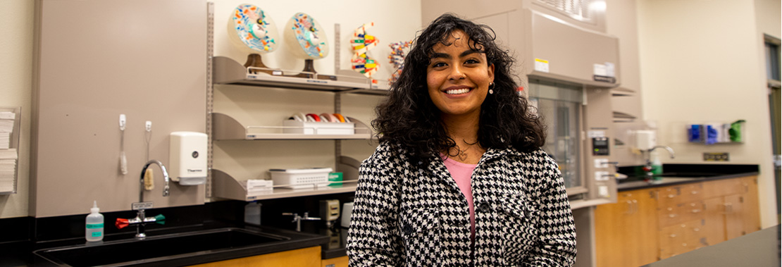 Briana Pomales stand smiling in a chemistry classroom