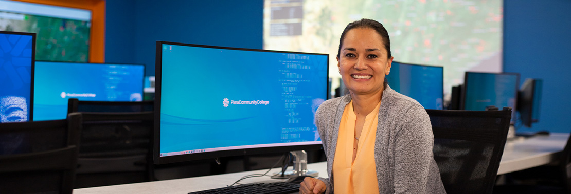 Tauty Sanchez sitting at a desk turned towards the camera and smiling. 