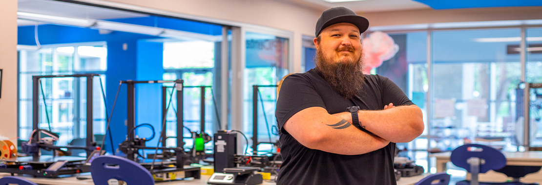 Marc Vaughn stands arms crossed with a grin in the Makerspace at East Campus