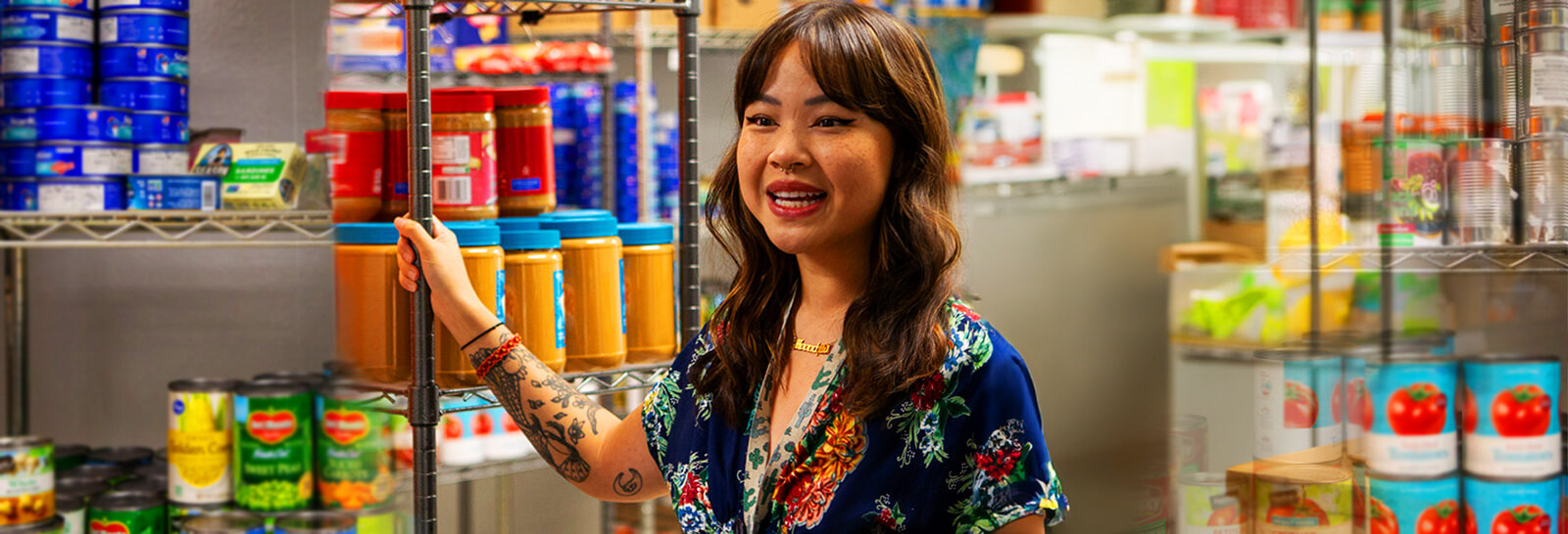 Susan Ho stands next to a shelf of grocery items at the ARC food pantry.