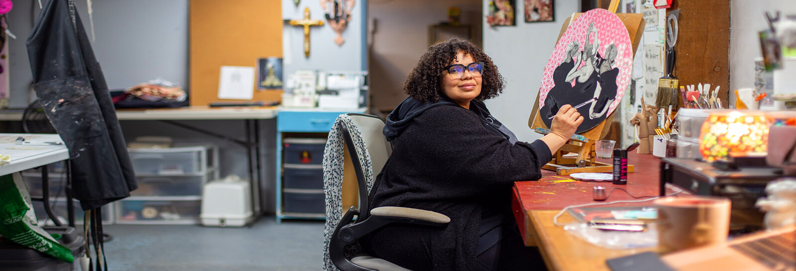 Lizz Denneau works in her studio smiling at the camera