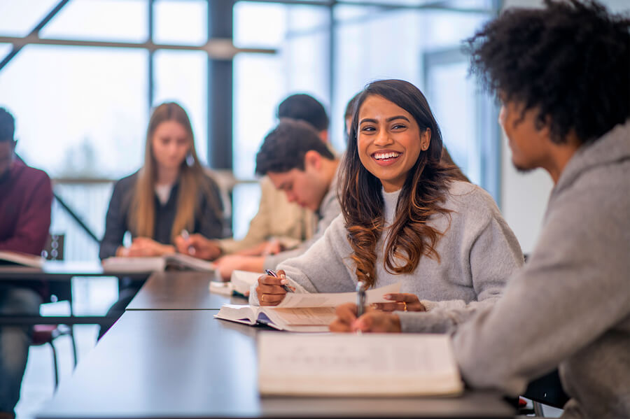 A student smiles during conversation with another student in a classroom