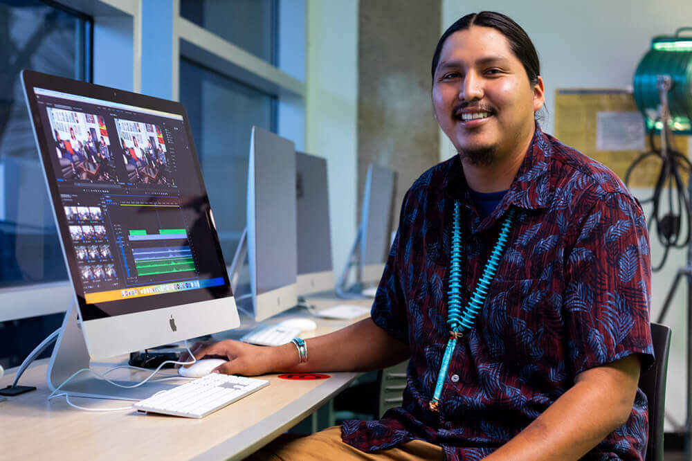 A student sits in front of a computer in a video arts lab