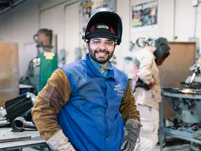 A student stands smiling in a welding class
