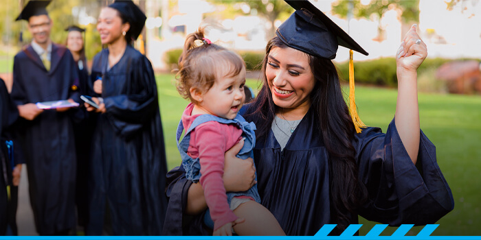 A parent-student holding their toddler during graduation. 