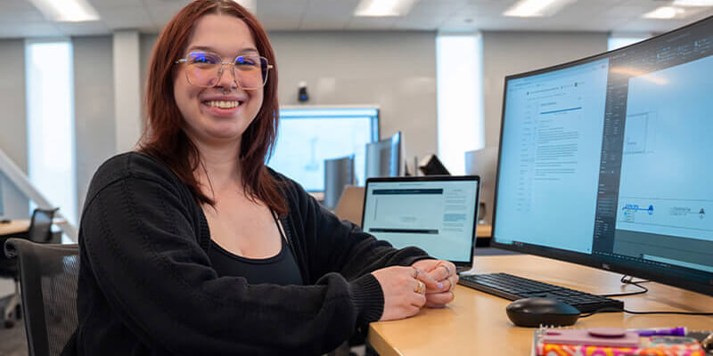 A female student smiles at a computer in a classroom