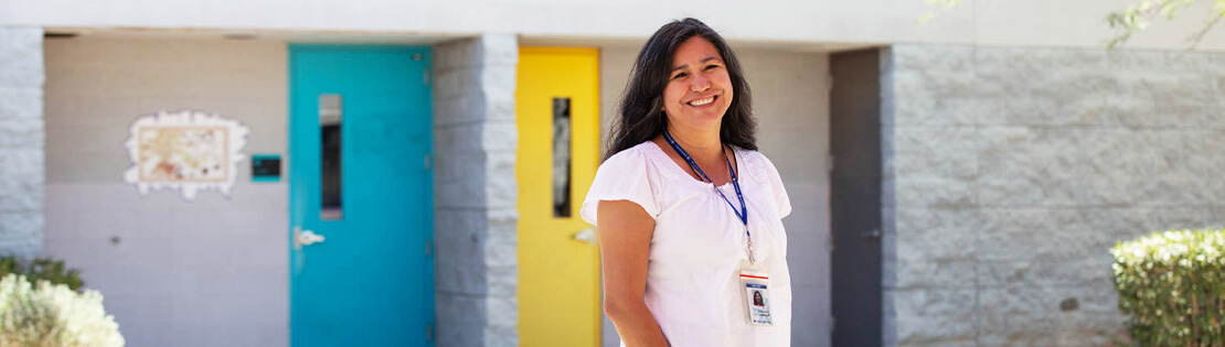 A Faculty Memebt Stands smiling in front of one of Pima's Adult Learning Center
