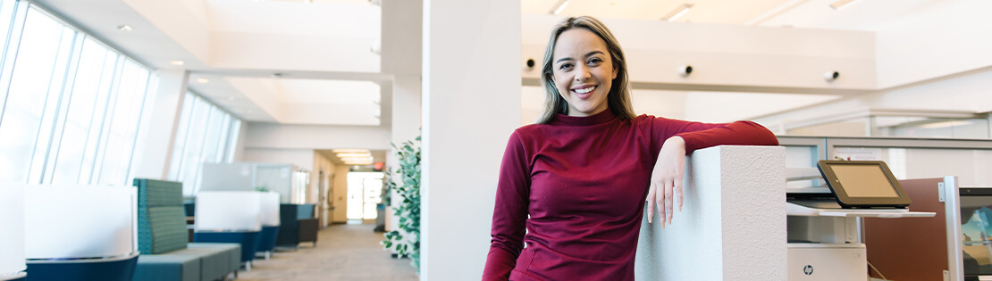 A student stands smiling leaning against a study cubicle in Pima's Desert Vista Campus Library