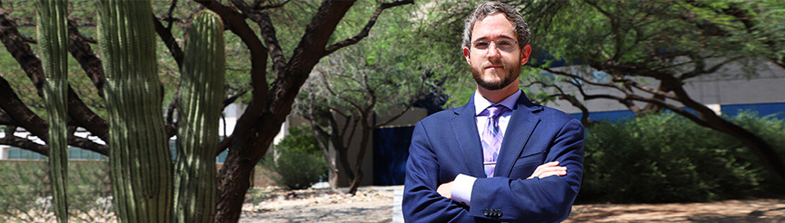 A paralegal student poses for a photo in a suit in a Pima West campus courtyard