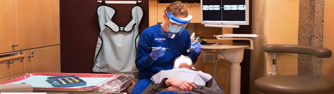A dental student works on another person at a dental clinic