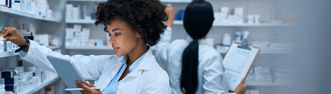 A pharmacy tech holds a clipboard and looks at a medicine bottle. 