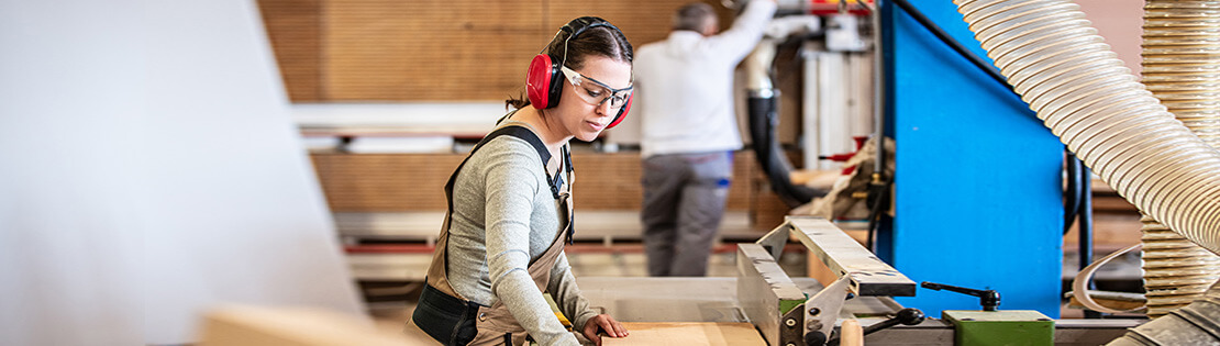 A student with safety equipment works on a saw table in a woodworking class