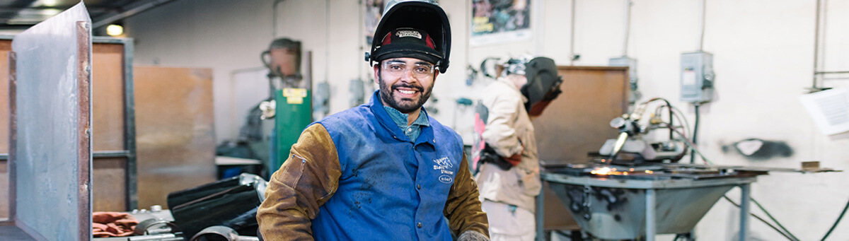 A student pauses and poses for a photo while working on welding project
