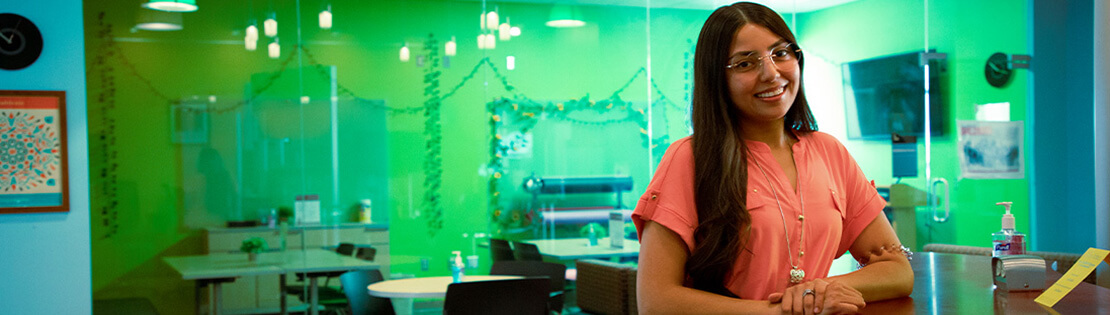 A student worker stands smiling in a student resource center at Pima's Northwest campus