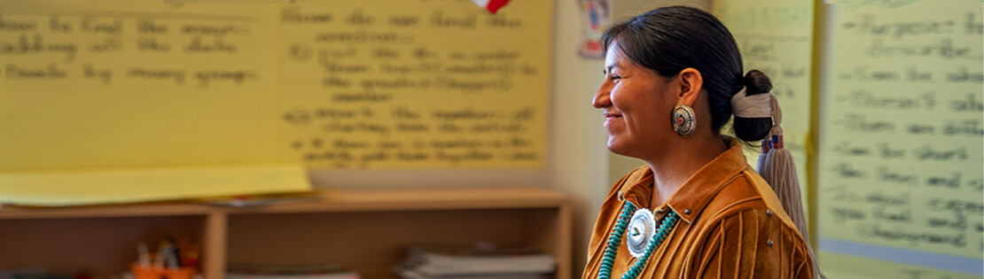 A Native American woman stands smiling in a Pima classroom