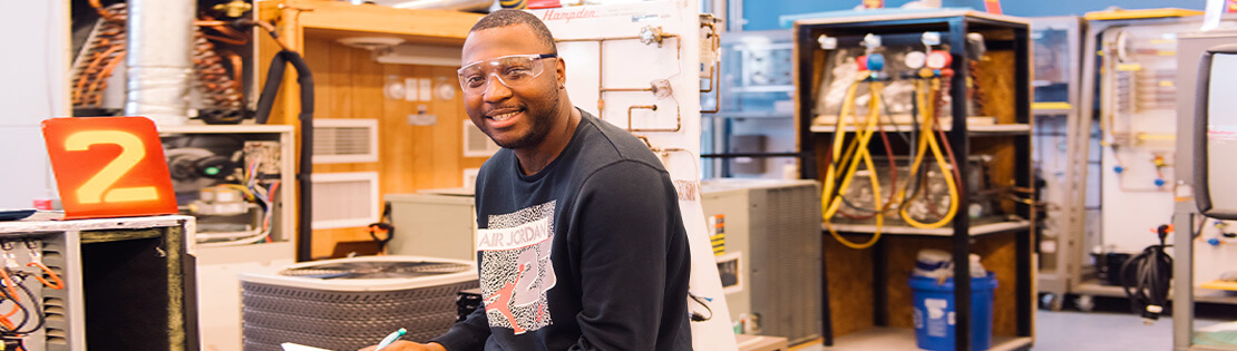 A student with safety glasses sits in a engineering class smiling