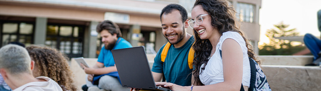 Students sit on stairs laughing while playing with a new laptop