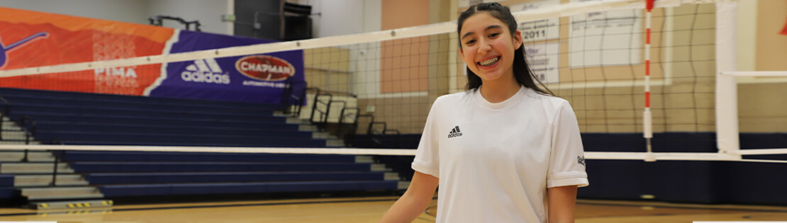 A Pima Volleyball Student Athlete poses smiling on the volleyball court at Pima's West Campus