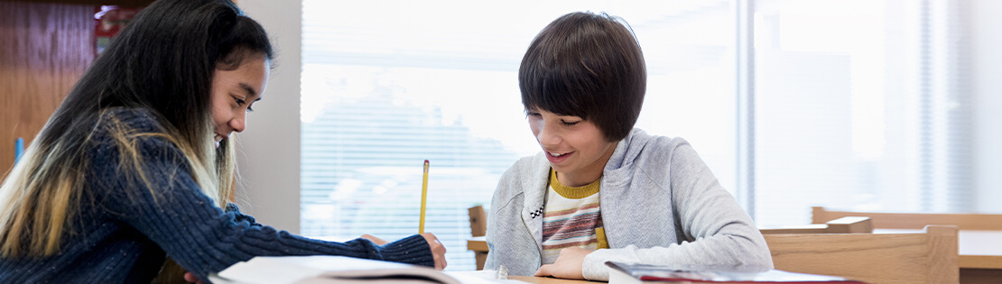 Two pre-teenaged children excitedly work together on a writing activity in a classroom