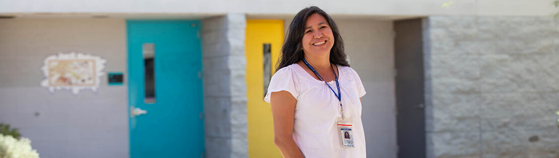 A faculty member stands smiling in front of classrooms