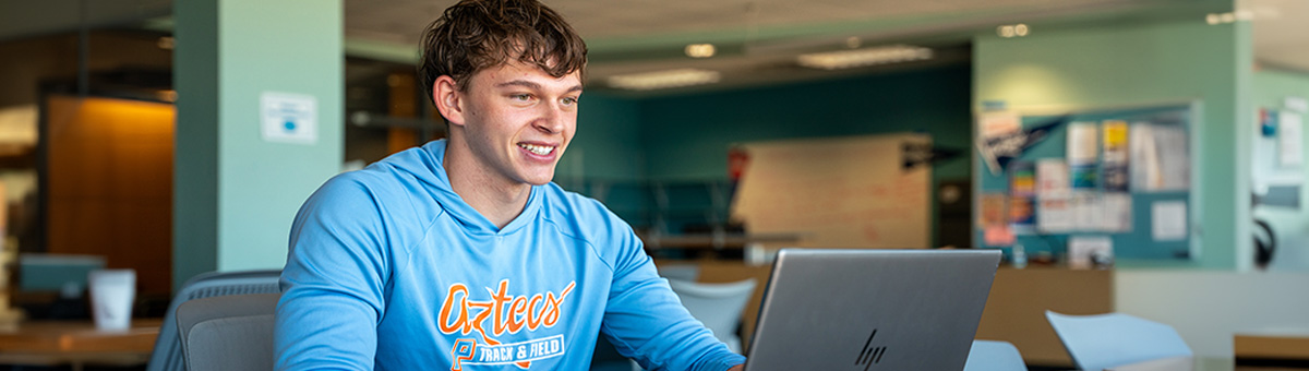 A students sit in front of a computer working on a project in a lounge