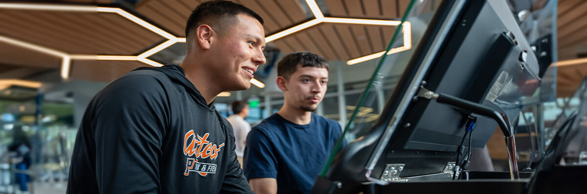 A pima student is shown something on a computer by a student worker