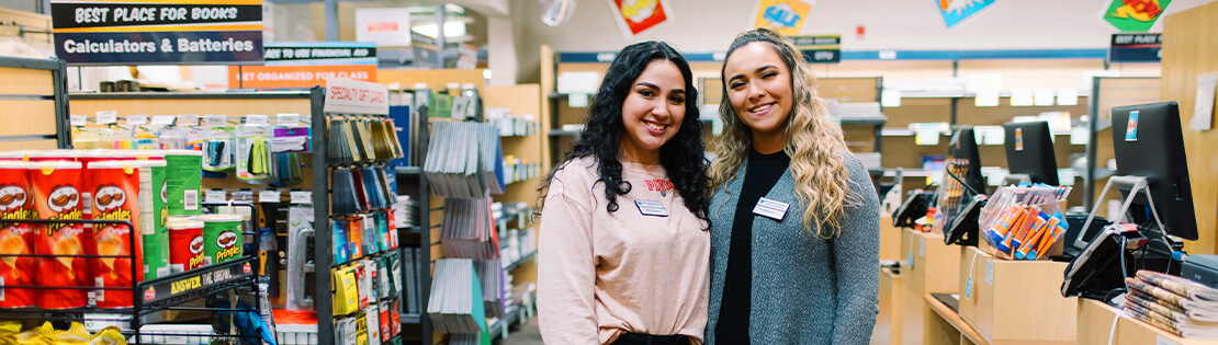 Two Student workers stand smiling in a Pima Bookstore
