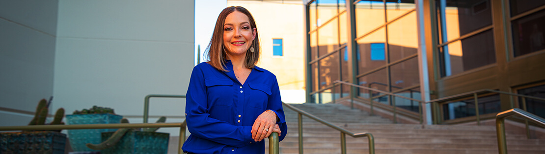 Professional woman smiles on steps of Northwest Campus in a blue blazer.