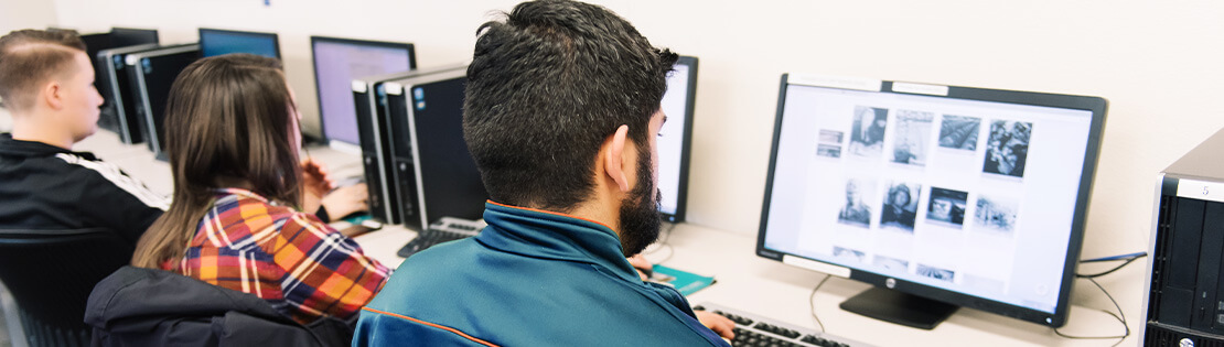 Two students sit a computers in a classroom, editing a student publication