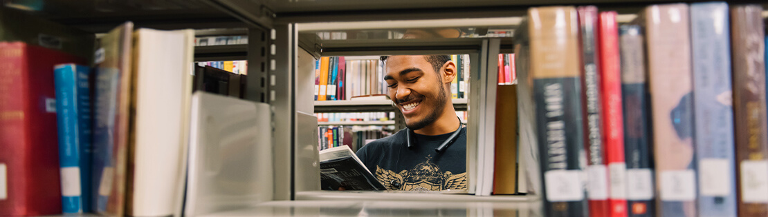 A student smiles while looking at a book in a Pima campus Library