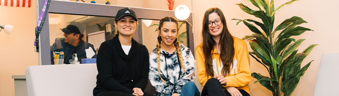 three students sit on a couch smiling in a Pima student services center