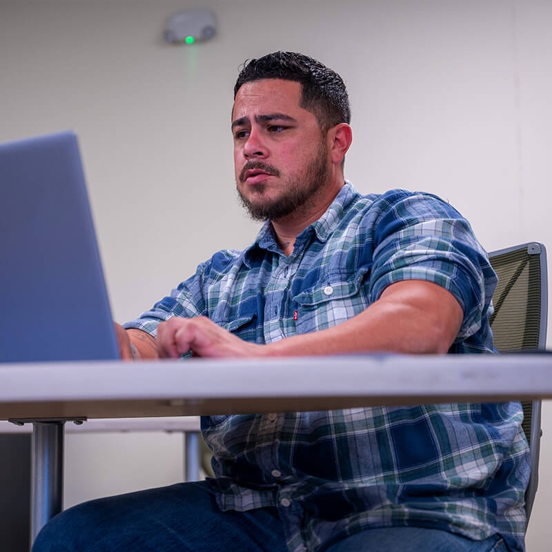 Luis sits in a classroom with a computes